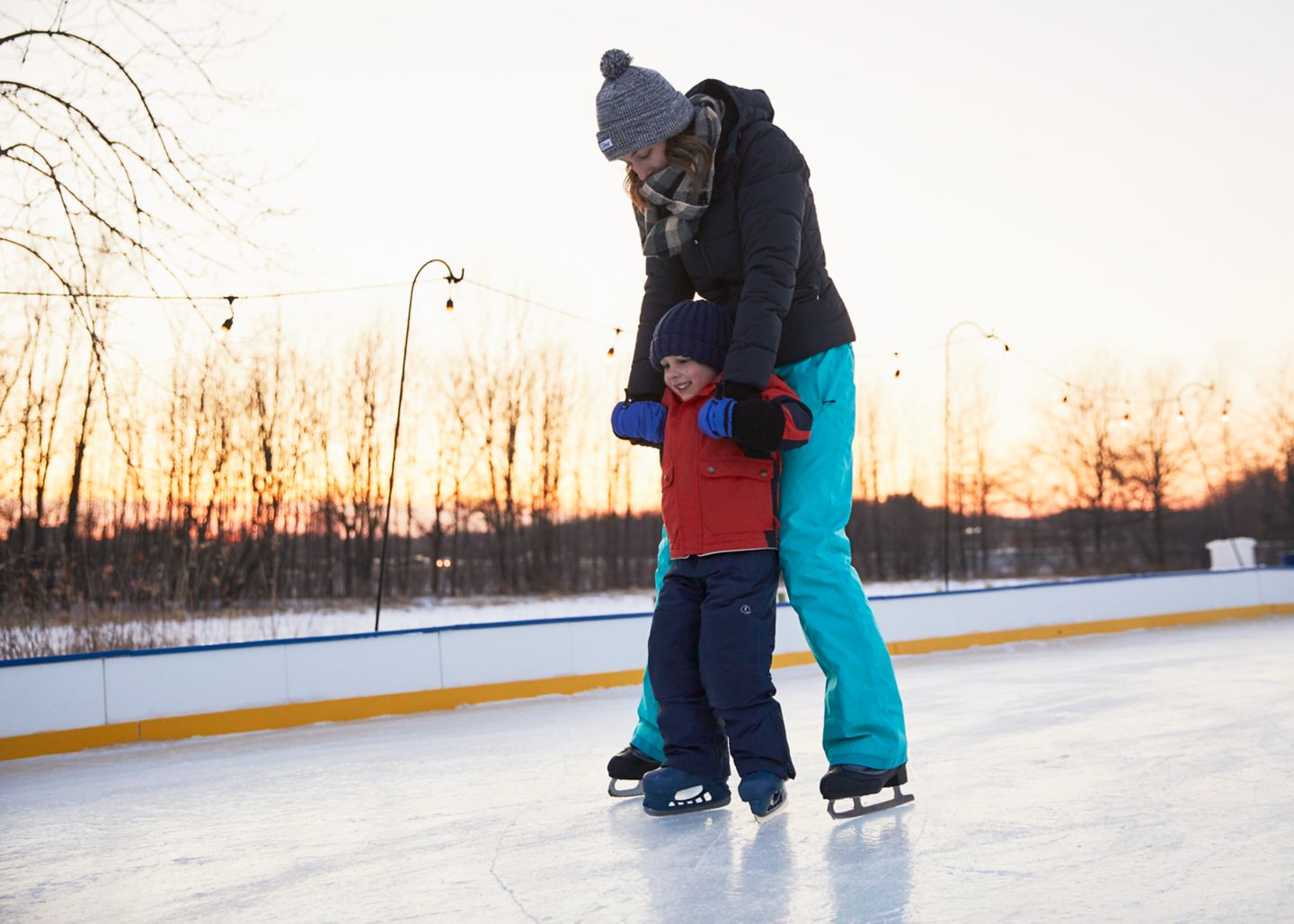 a mother and son iceskating on an outdoor rink with the sun setting in the background