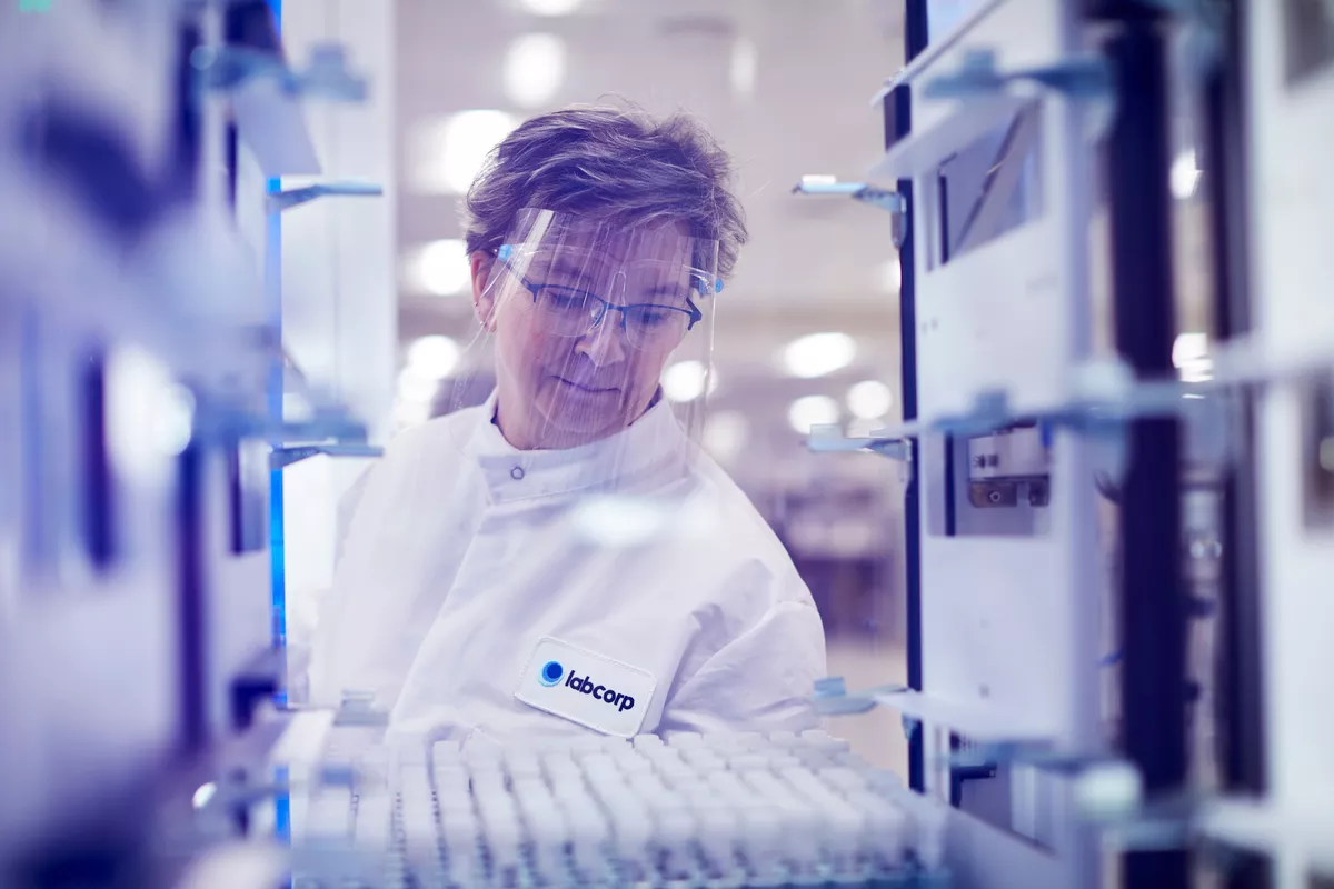 Labcorp scientist wearing PPE placing tray of samples in fridge