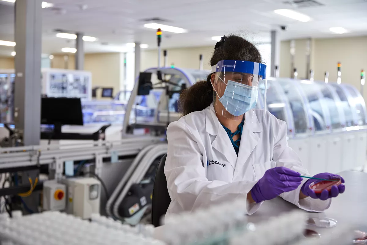 Eine Labcorp-Wissenschaftlerin in Schutzausrüstung mit einer Petrischale in der Hand