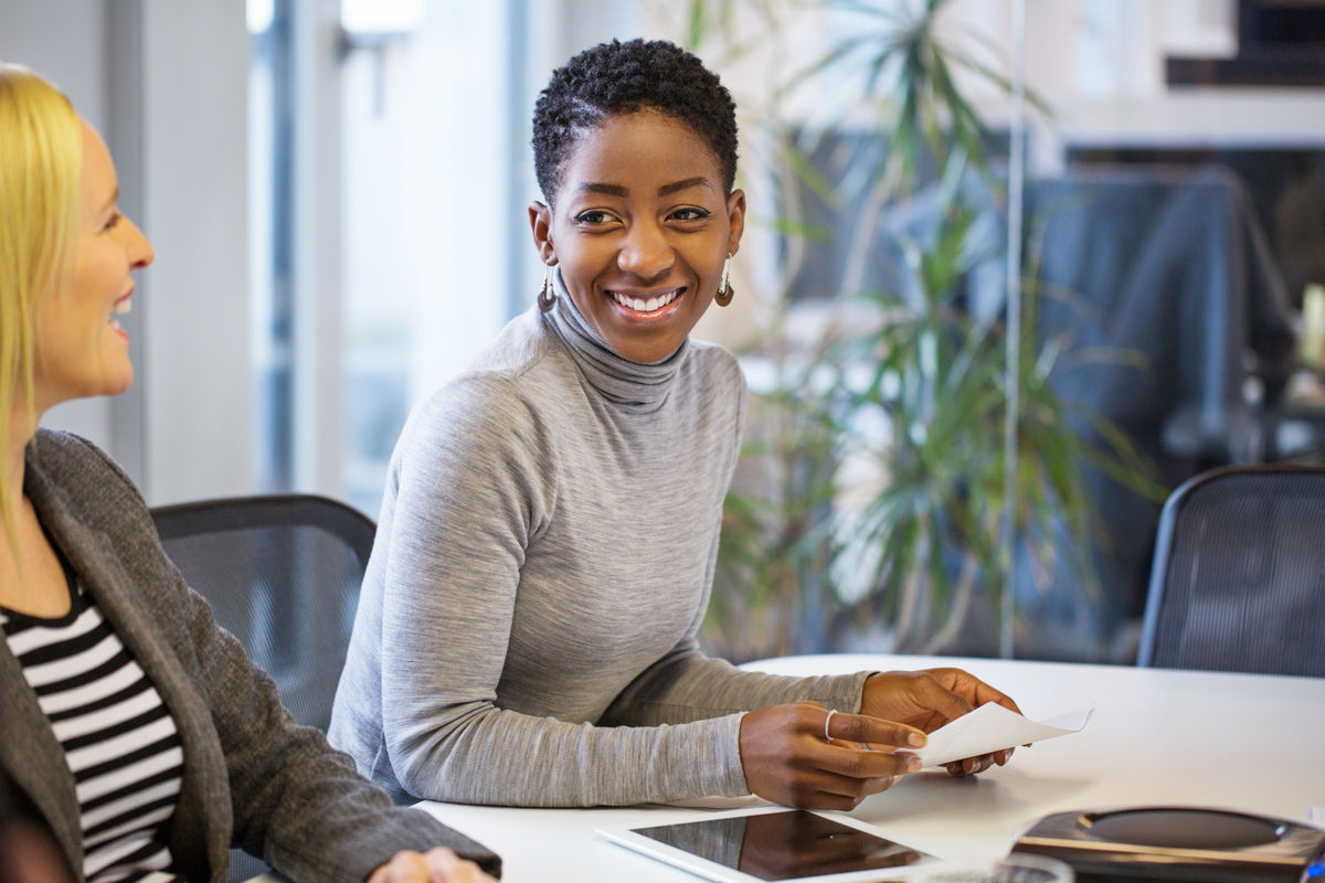 Two women sitting in an office setting. They are both laughing