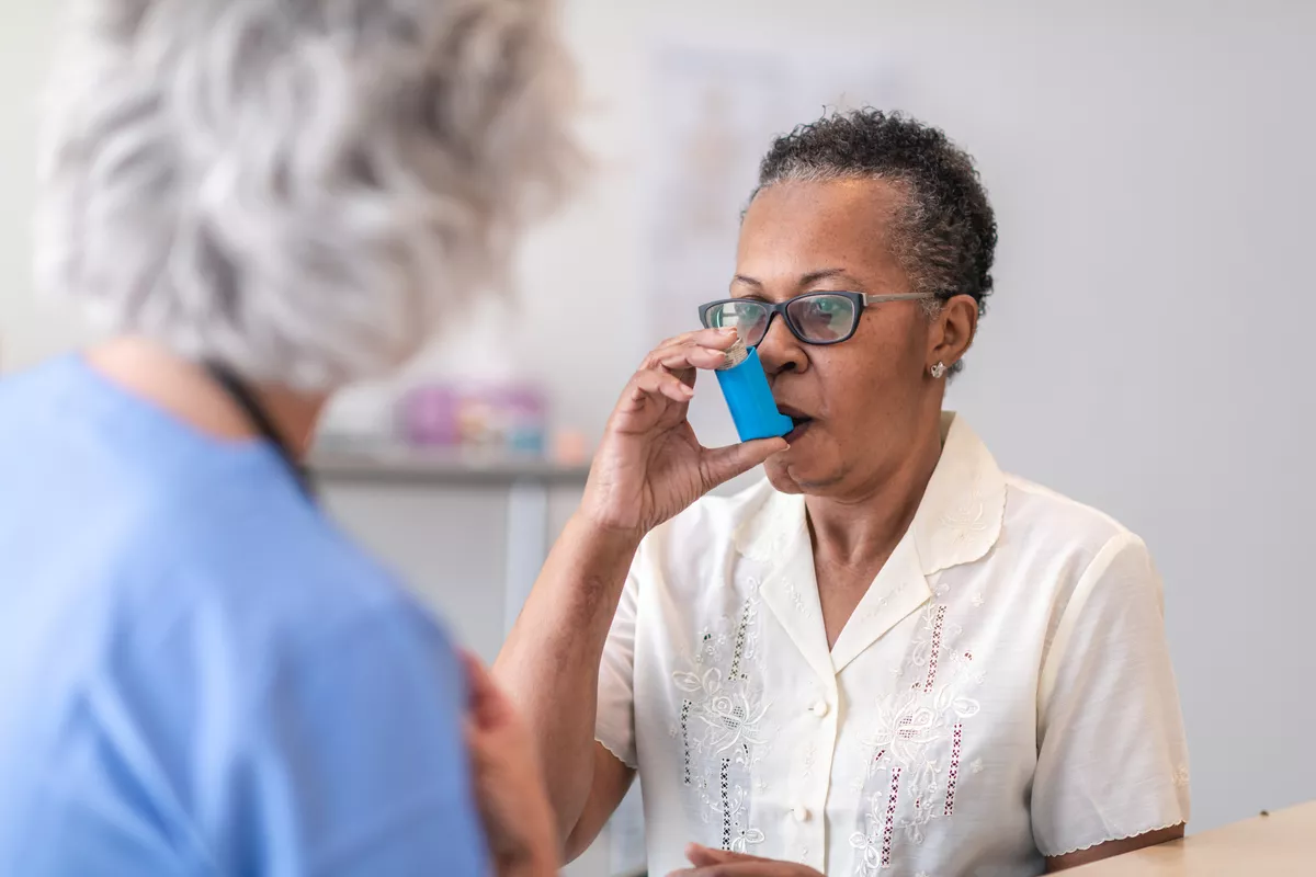 Older patient taking a puff from an inhaler with provider in the foreground