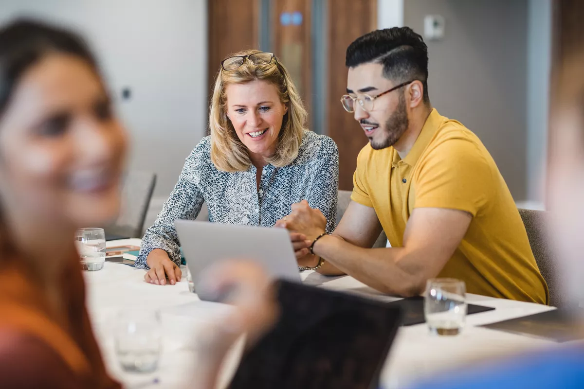 three people in a meeting while two that are in focus look at a screen