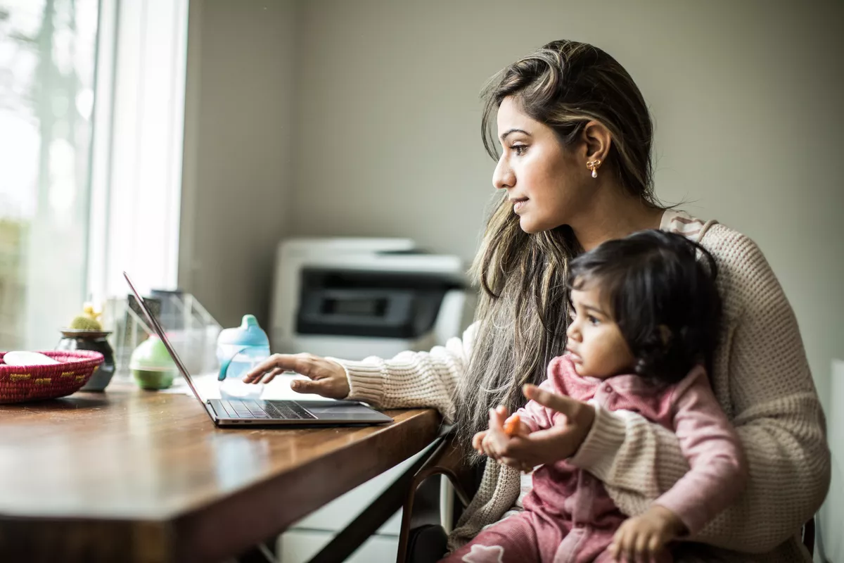 Mother holding her daughter while she is typing on her computer