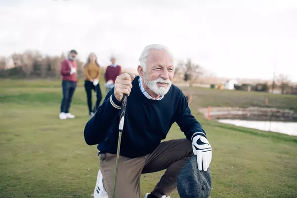 Older man kneeling down on a golf course. He is navigating the green