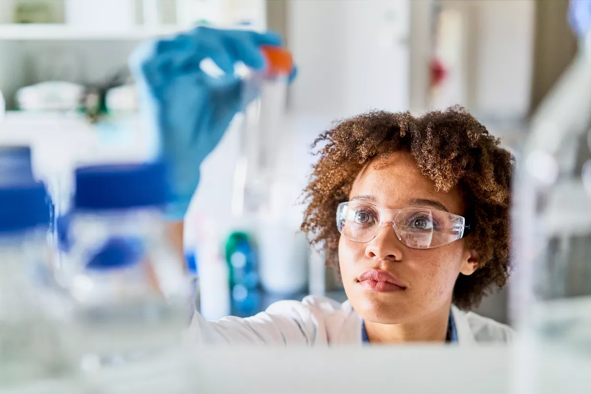 Image of a scientist holding up a vail. She is observing the specimen inside