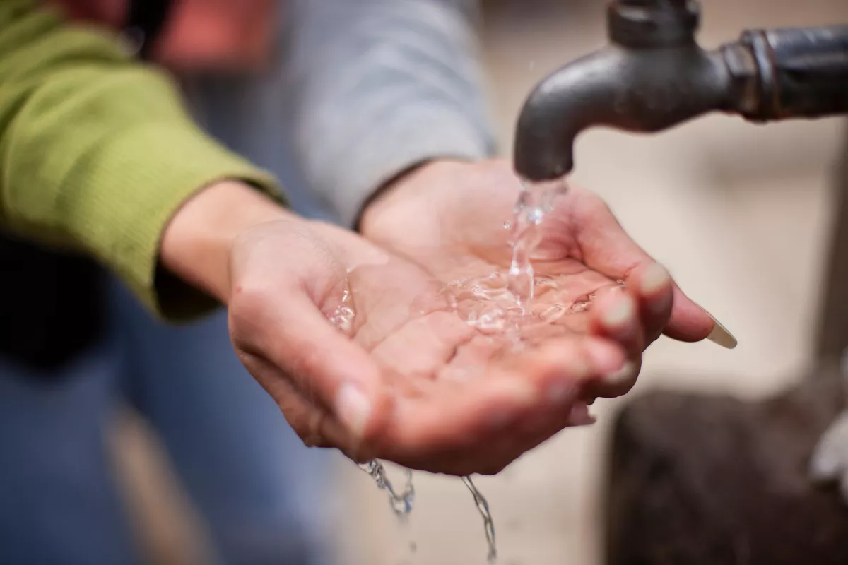Hands rinsing down water as it comes from faucet