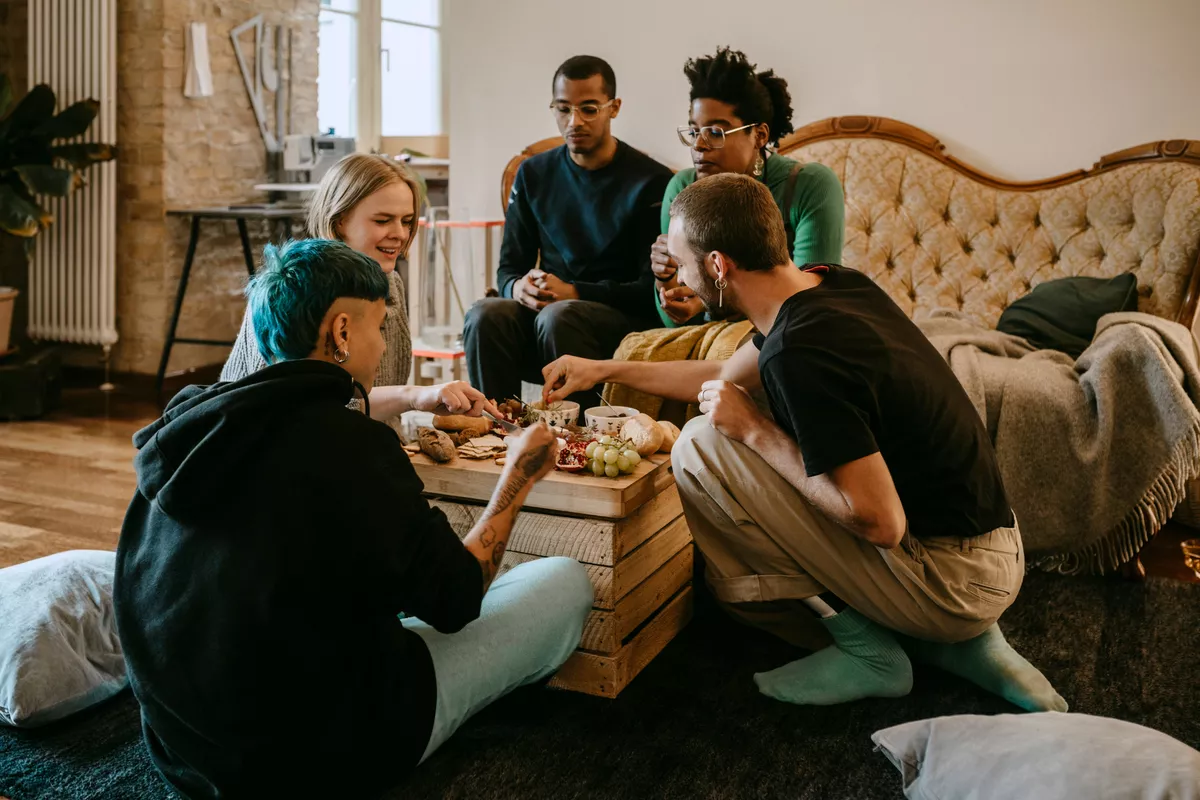 Group of five diverse friends sitting in a living room eating dinner