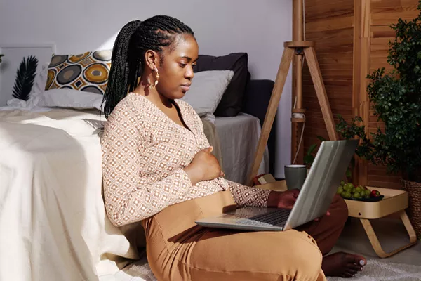 Pregnant woman sitting on the floor looking at her laptop screen