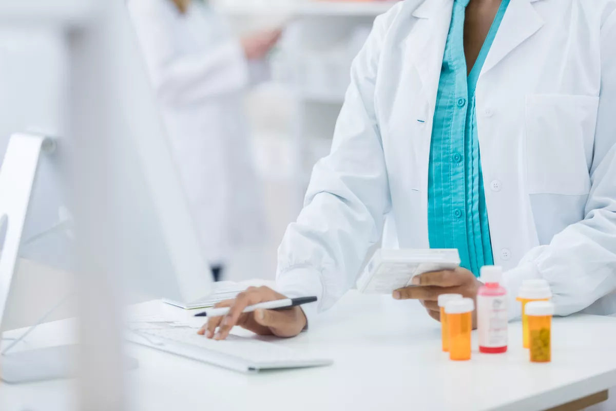 pharmacist working at a computer. There are multiple pill bottles on the desk