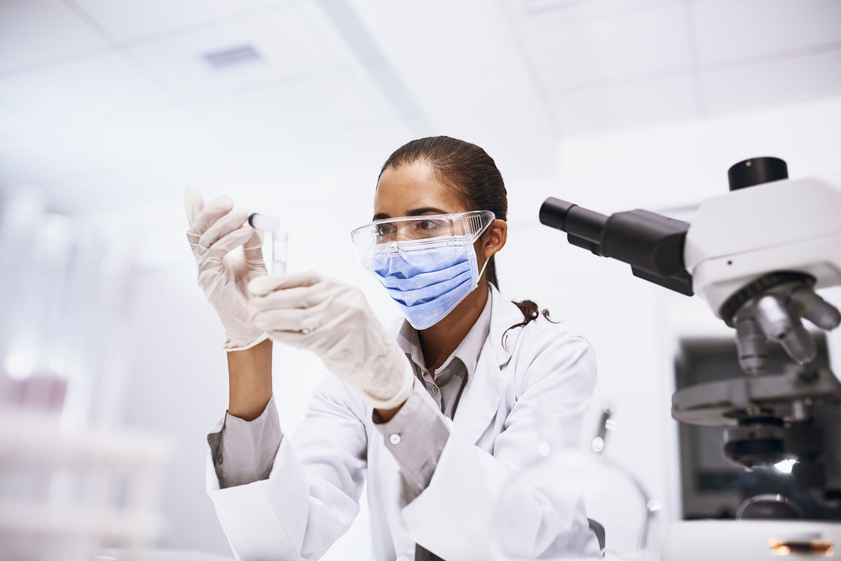 scientist sitting next to a microscope wearing PPE. She is diluting a sample to research