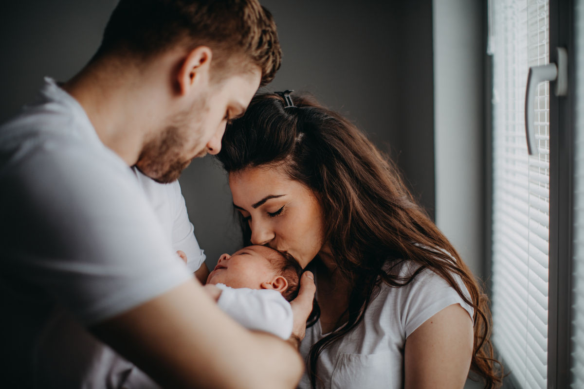 Mother and father embracing their baby. The mother is kissing the baby's head