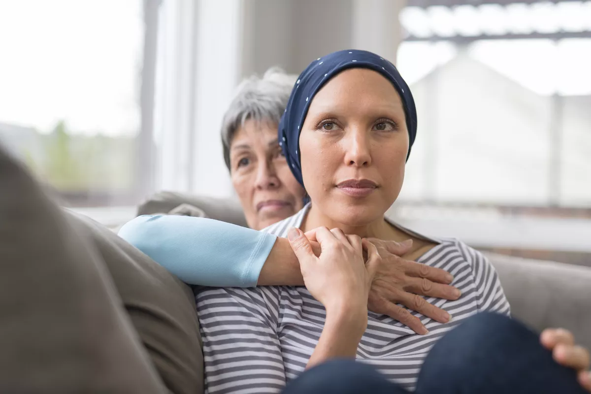 Mother embracing her daughter that has cancer on a couch