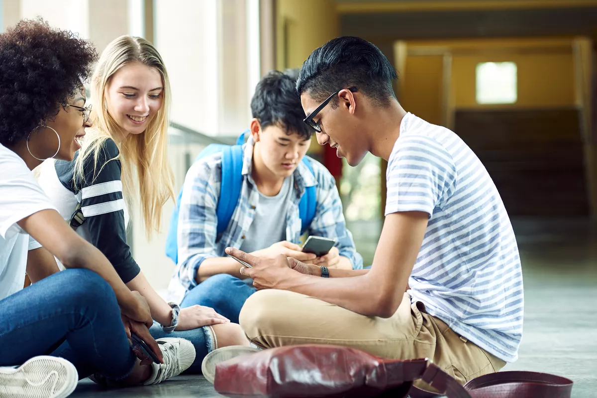 Group of four young and diverse friends sitting on the ground tallking to each other