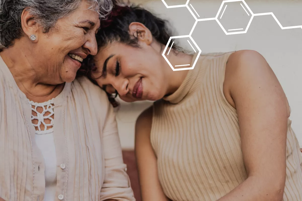 Older woman and younger woman sitting down. The younger woman has her head on the older woman's shoulder. There is a chemical molecule on the top right 