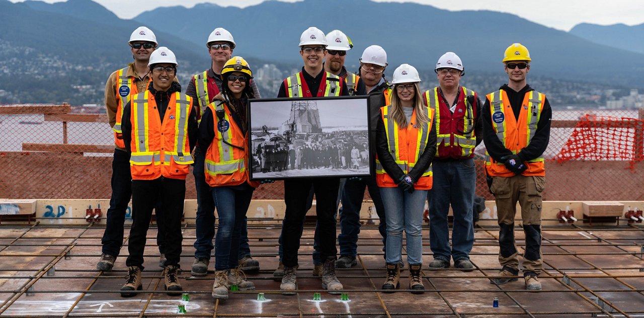 Staff wearing safety gear h olding old photo of facility