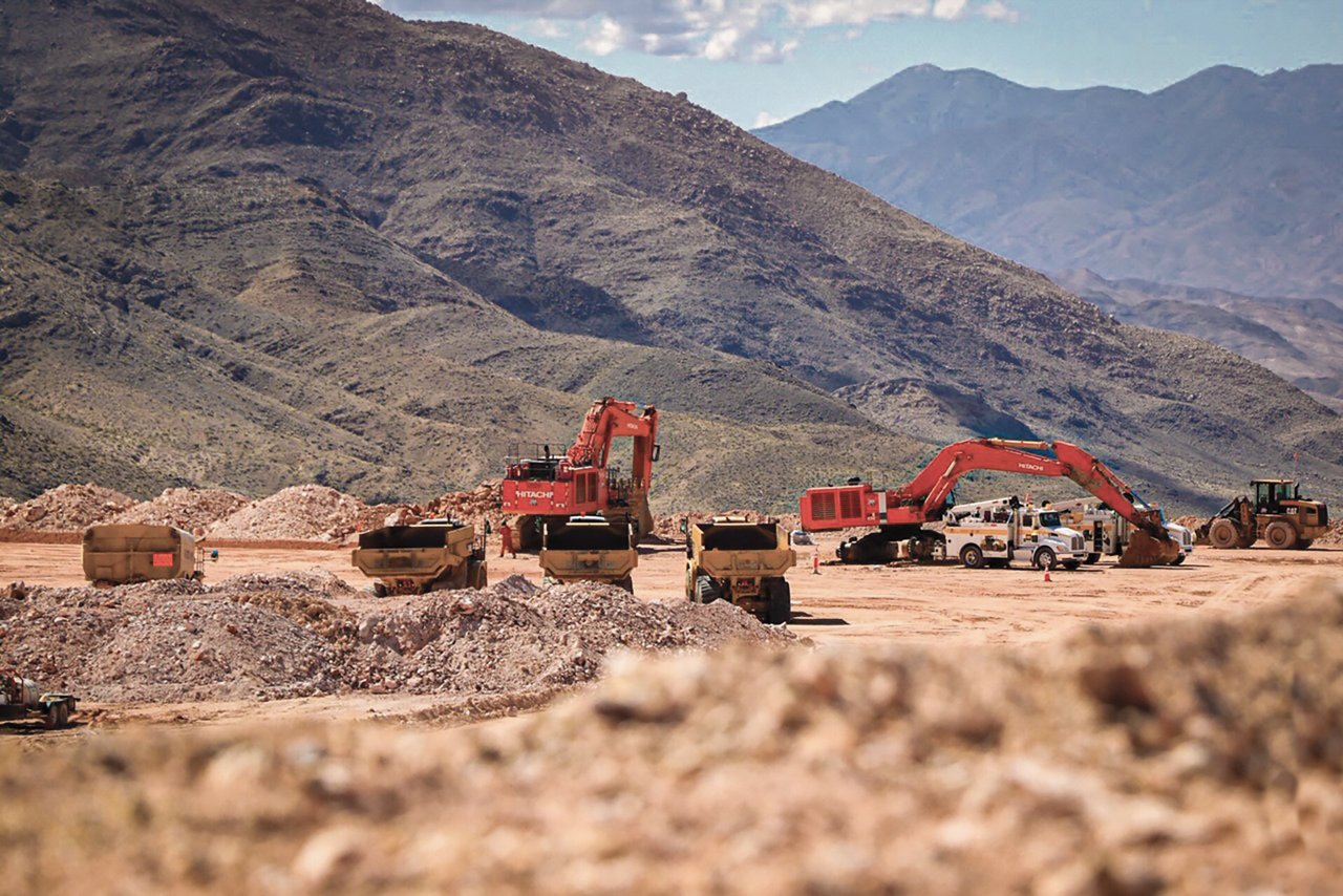 Machines digging dirt in front of hills of dirt