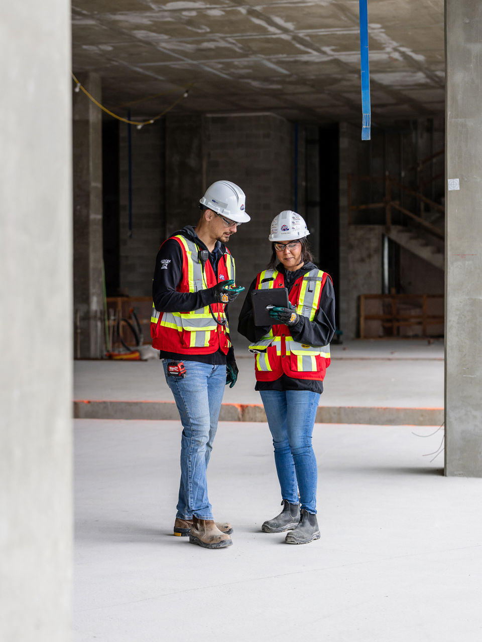 Construction workers wearing safety helmet and jacket looking at device