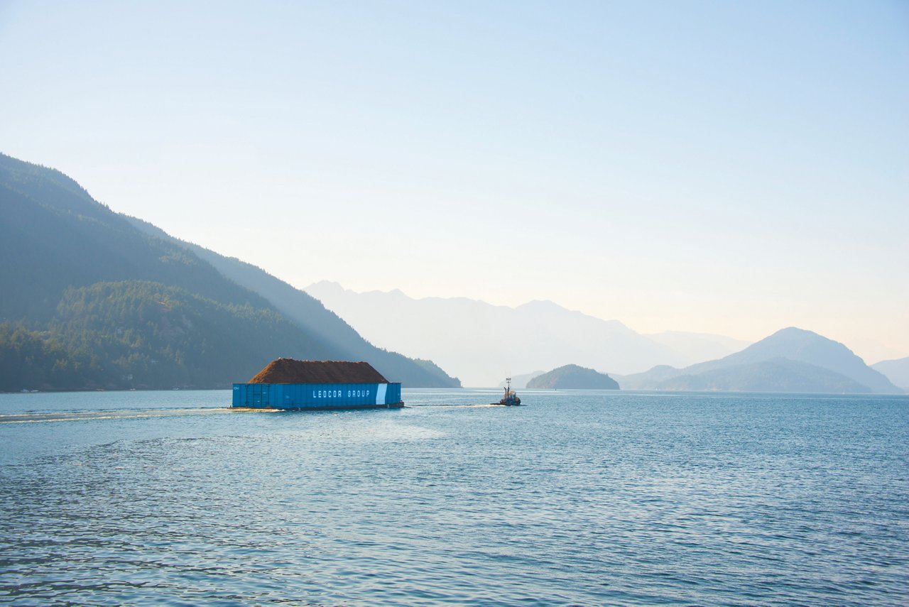 Tug boat pulling dirt payload across lake