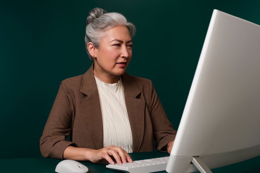 Woman sitting in her office at a dark green desk working on her computer and looking at the screen.