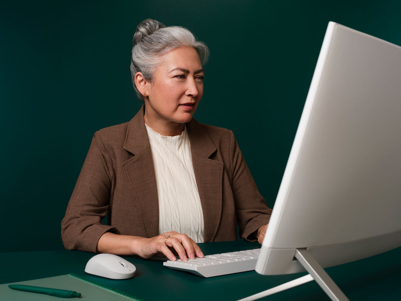 Femme assise à son bureau, à un bureau vert foncé, travaillant sur son ordinateur et regardant l'écran.