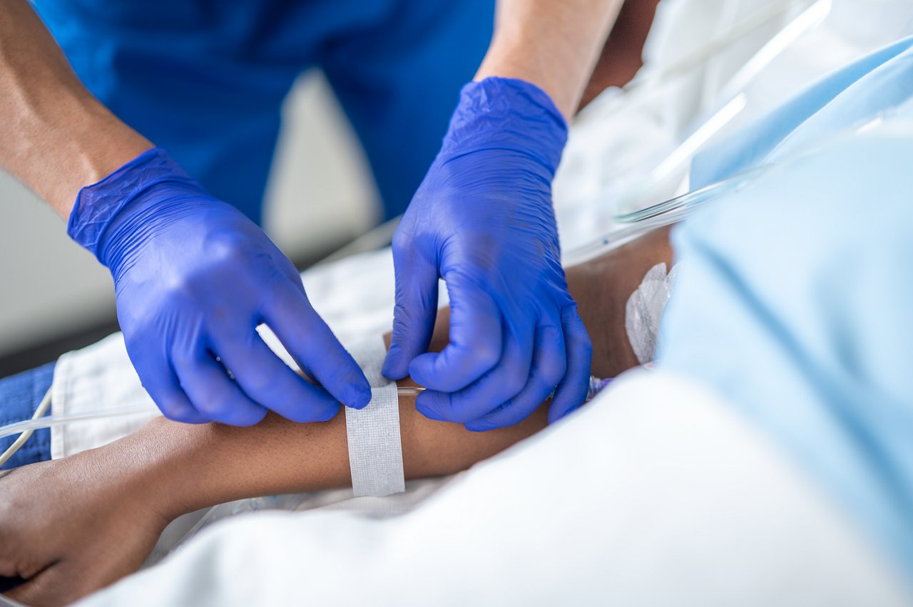 Patient in hospital with nursing staff  applying Micropore S medical tape to IV line