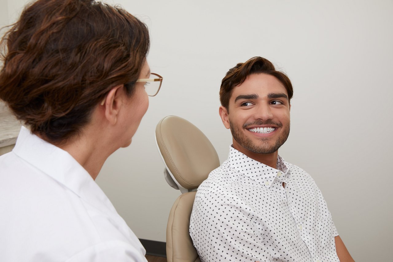 A man in a dental chair smiles at a dentist whose back is to the camera