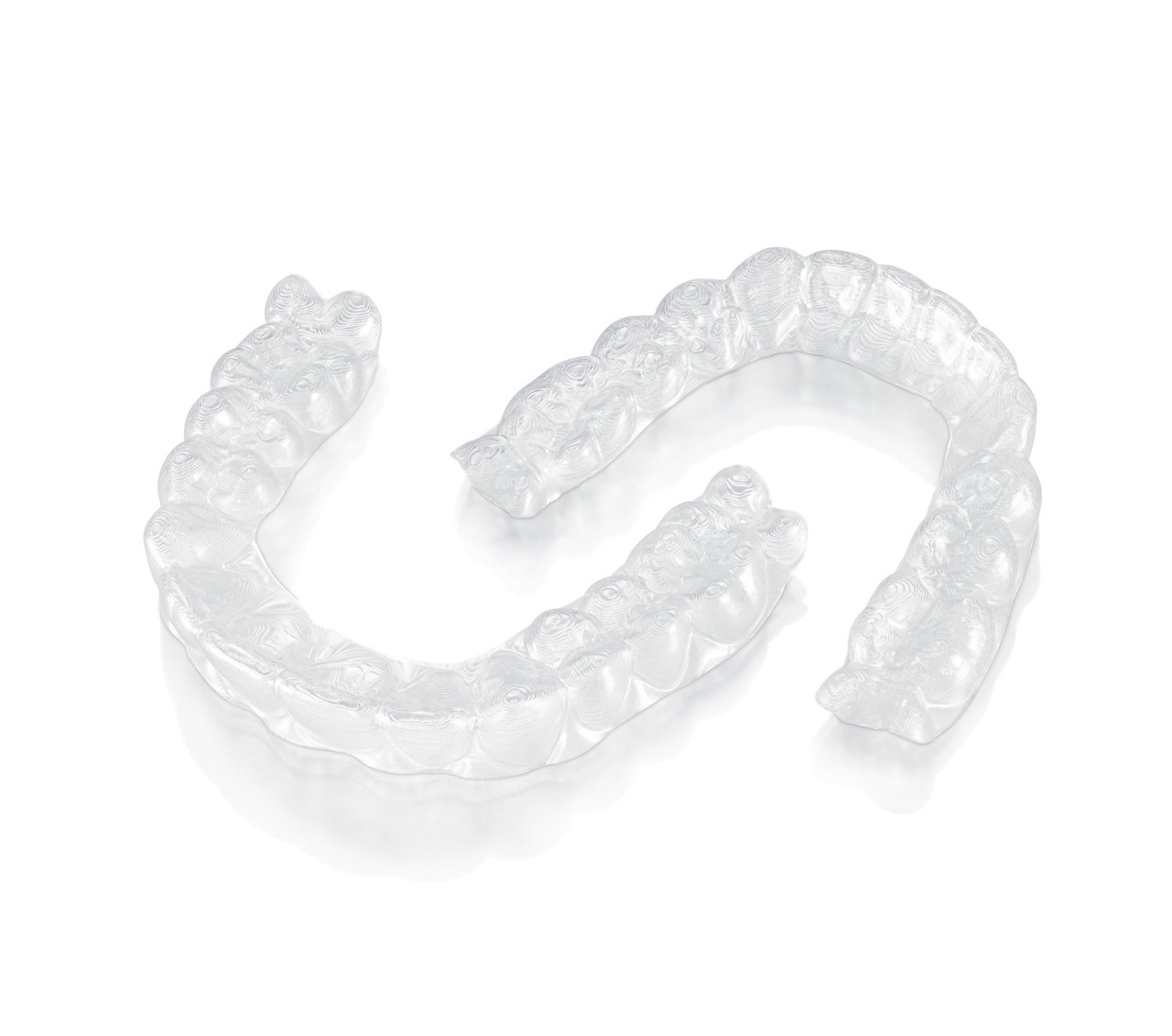 Photo of 3M™ Clarity™ Aligners on a white background and laying down outside of the case.