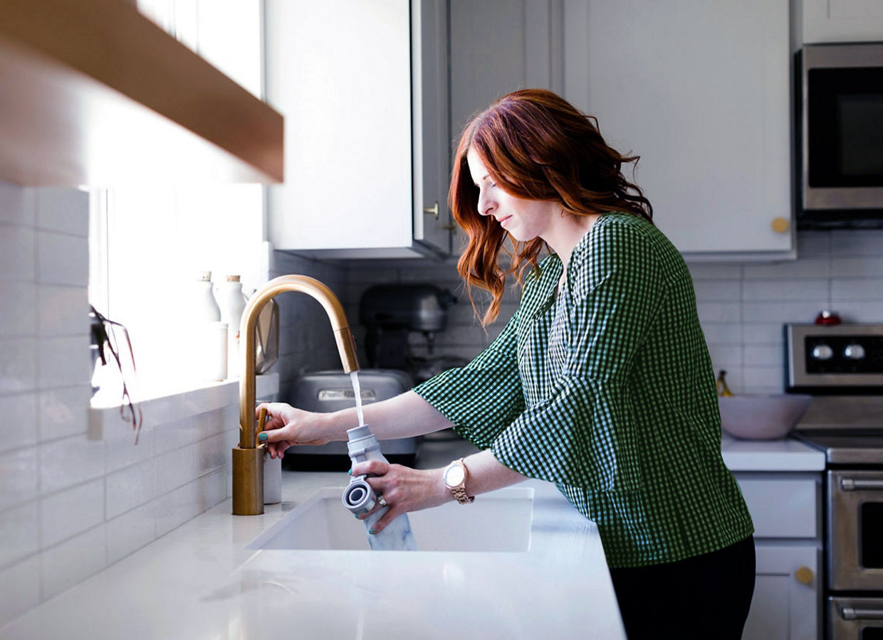 Woman filling water bottle in kitchen sink, Salt Lake City, Utah, North America