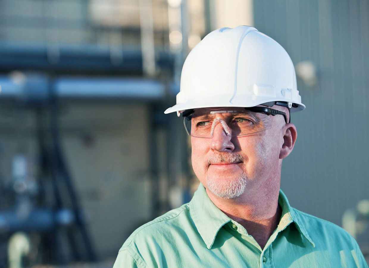 Close-up of a thoughtful engineer wearing a hard hat, looking away while standing at a construction site.
