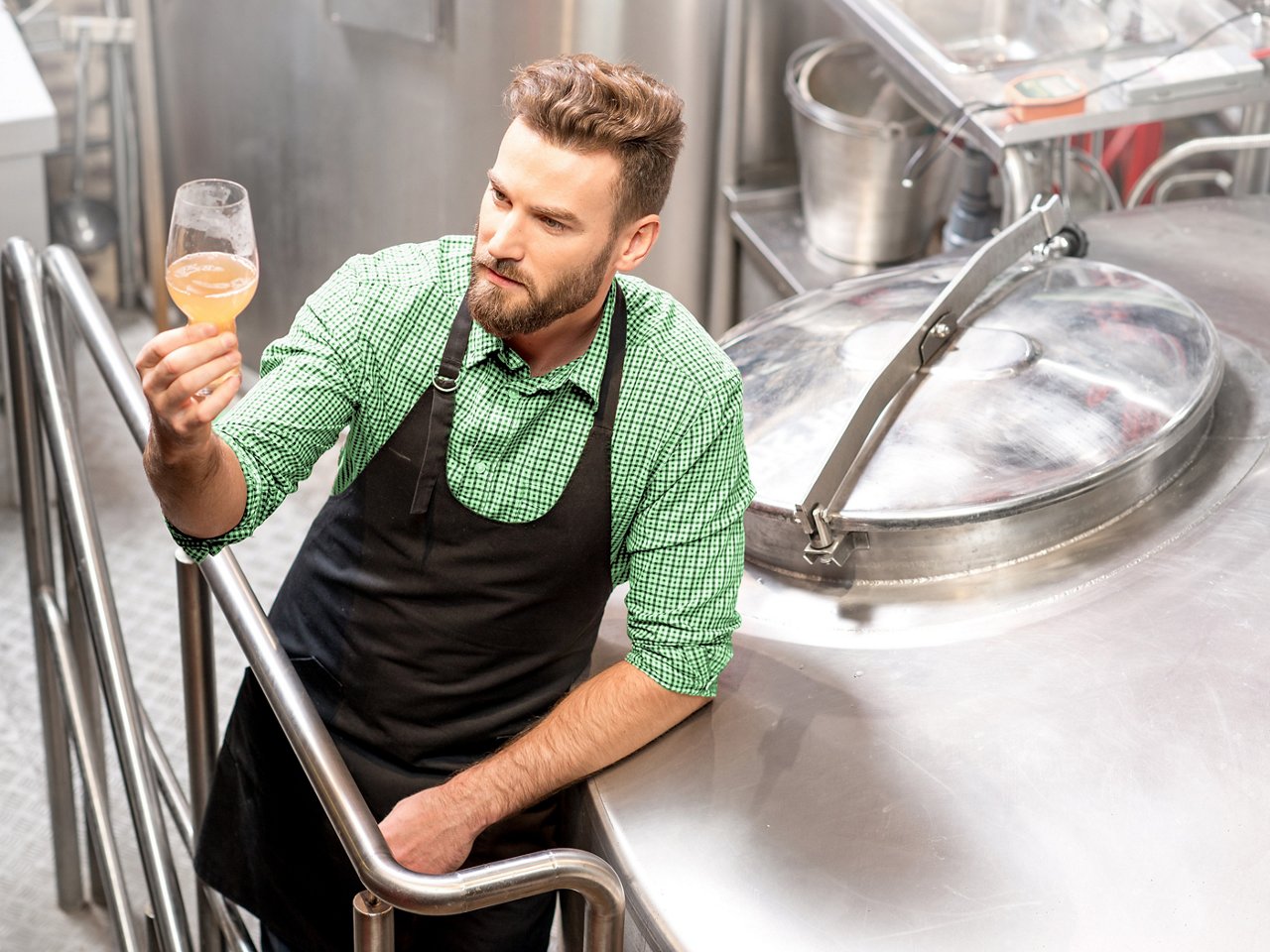 Brewer checking the quality of the beer wort near the metal containers at the manufacturing site