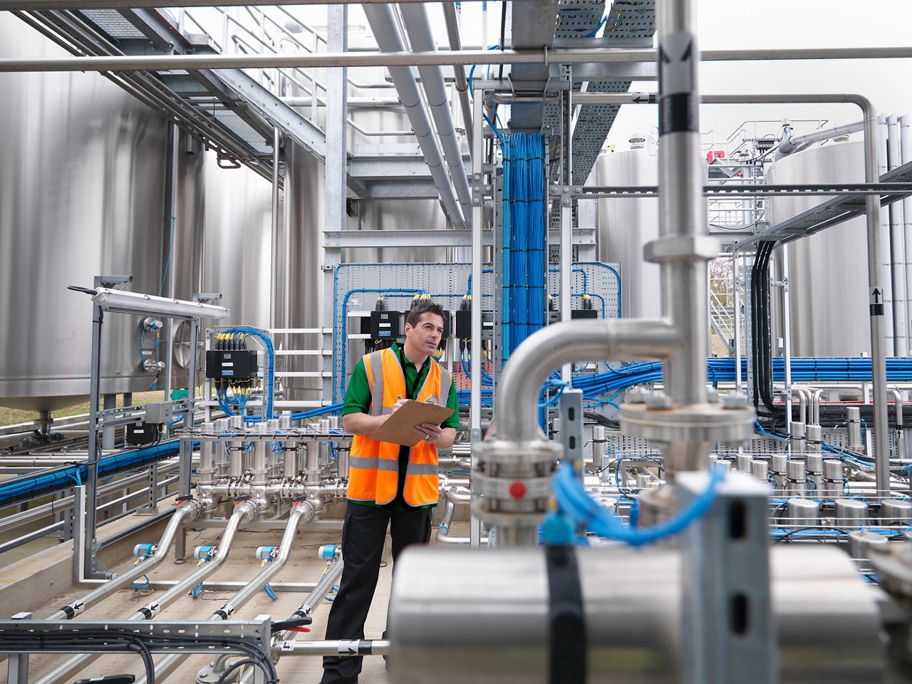 Man in an orange safety vest holding a clipboard inspects pipes