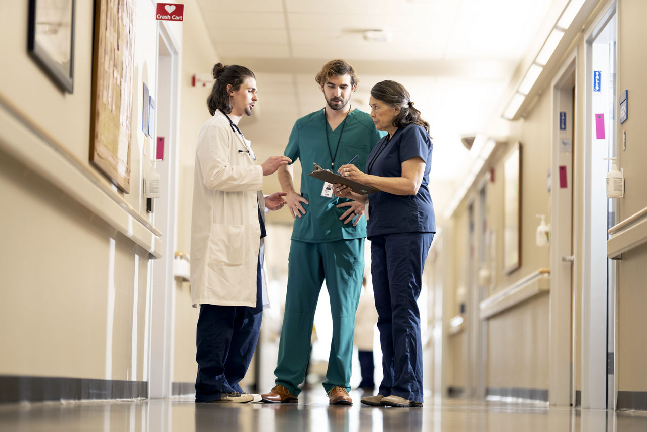 Male doctor with nurses talking in a hospital hallways while looking at a chart.
