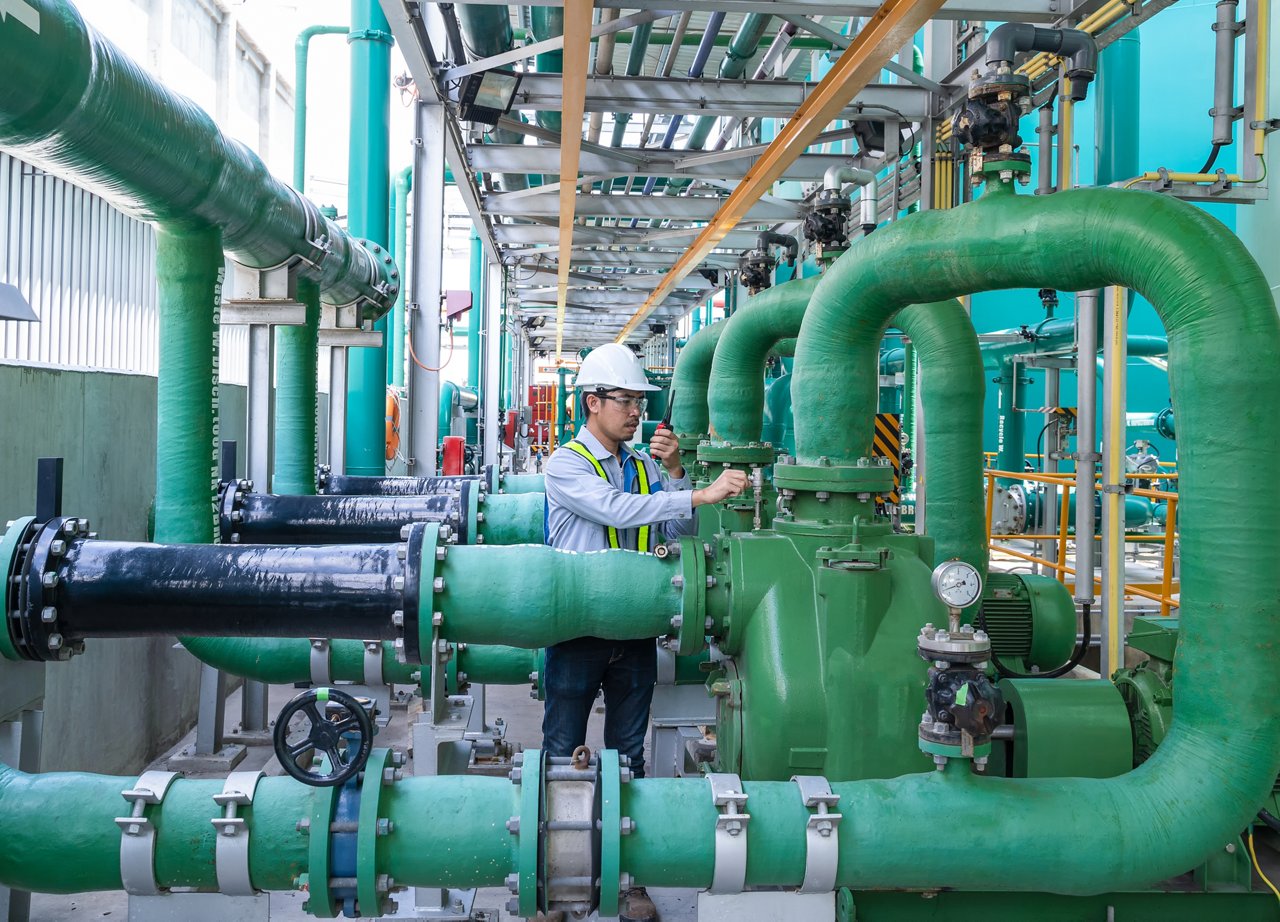 Asian male engineer working at factory with pipeline and pump.operator operation of oil and gas process at power plant, operator monitor production process, routine daily work ,water pipe.