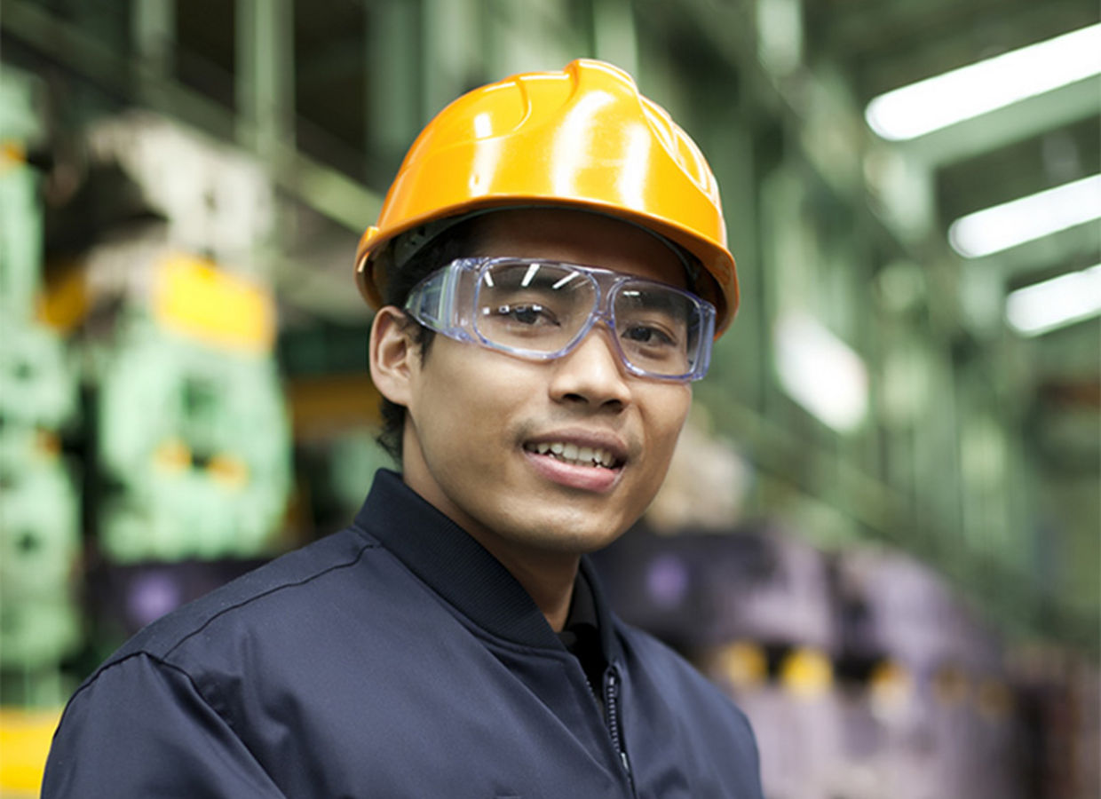 Portrait of an Asian engineer wearing a yellow hardhat, holding a clipboard.