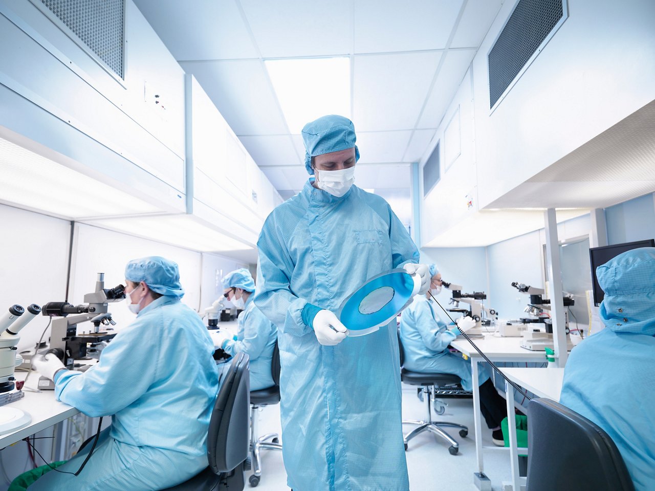 Electronics worker in clean room holding silicon wafer