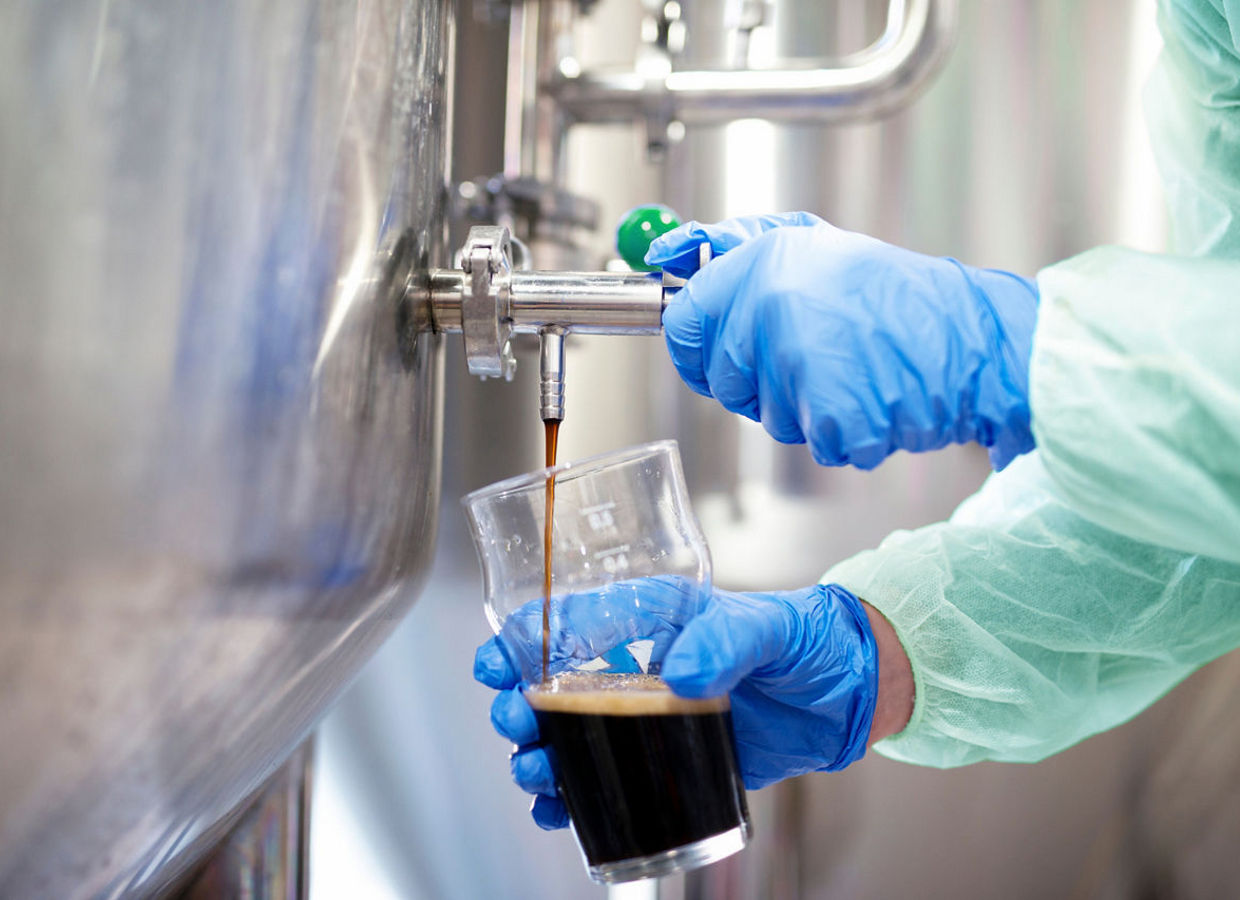 在釀酒廠的特寫，啤酒正在注入玻璃杯中。啤酒從水龍頭儲罐流出。技術員進行品質控制。