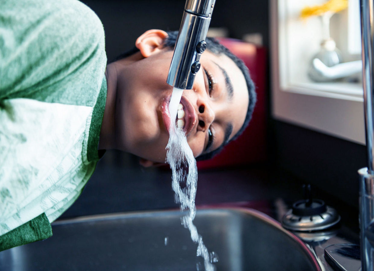 Child afro american boy take water on his mouth and drink in a kitchen