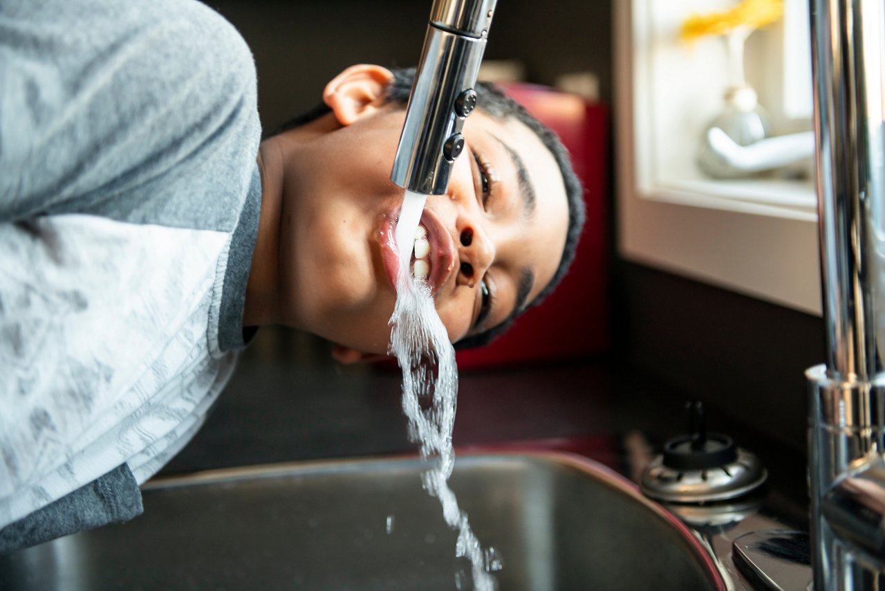 This asset is Shutterstock ID 1386055469. This is licensed from Shutterstock Images. Unlimited seats were licensed there is no charge to use this image. Please download and use as needed, but relate this asset to the final assets utilizing this image. Title: Child afro american boy take water on his mouth and drink in a kitchen