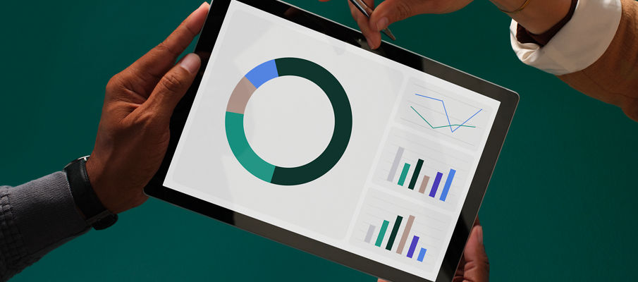 Male hands hold a tablet with colorful graphs and charts on the screen, while a woman's hand holding a stylus pen reaches over to point at the screen, all on a dark green background.
