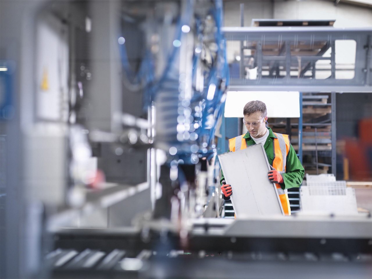 Worker inspecting parts next to robotic metal cutting machine in sheet metal factory