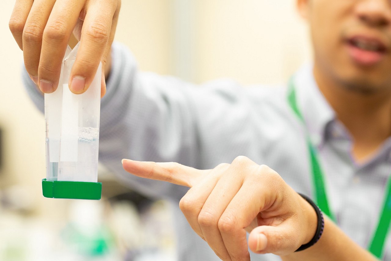 One scientist’s hand holding two vials while another points at the contents.