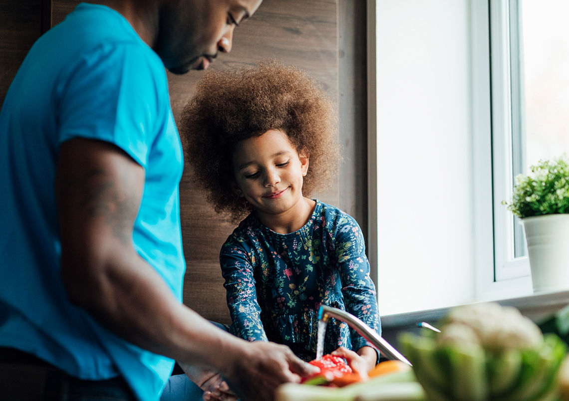Father and young daughter washing food in the kitchen sink.