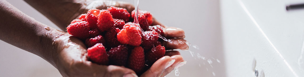 Close up rinsing raspberries in woman's hands under running water in the kitchen sink.