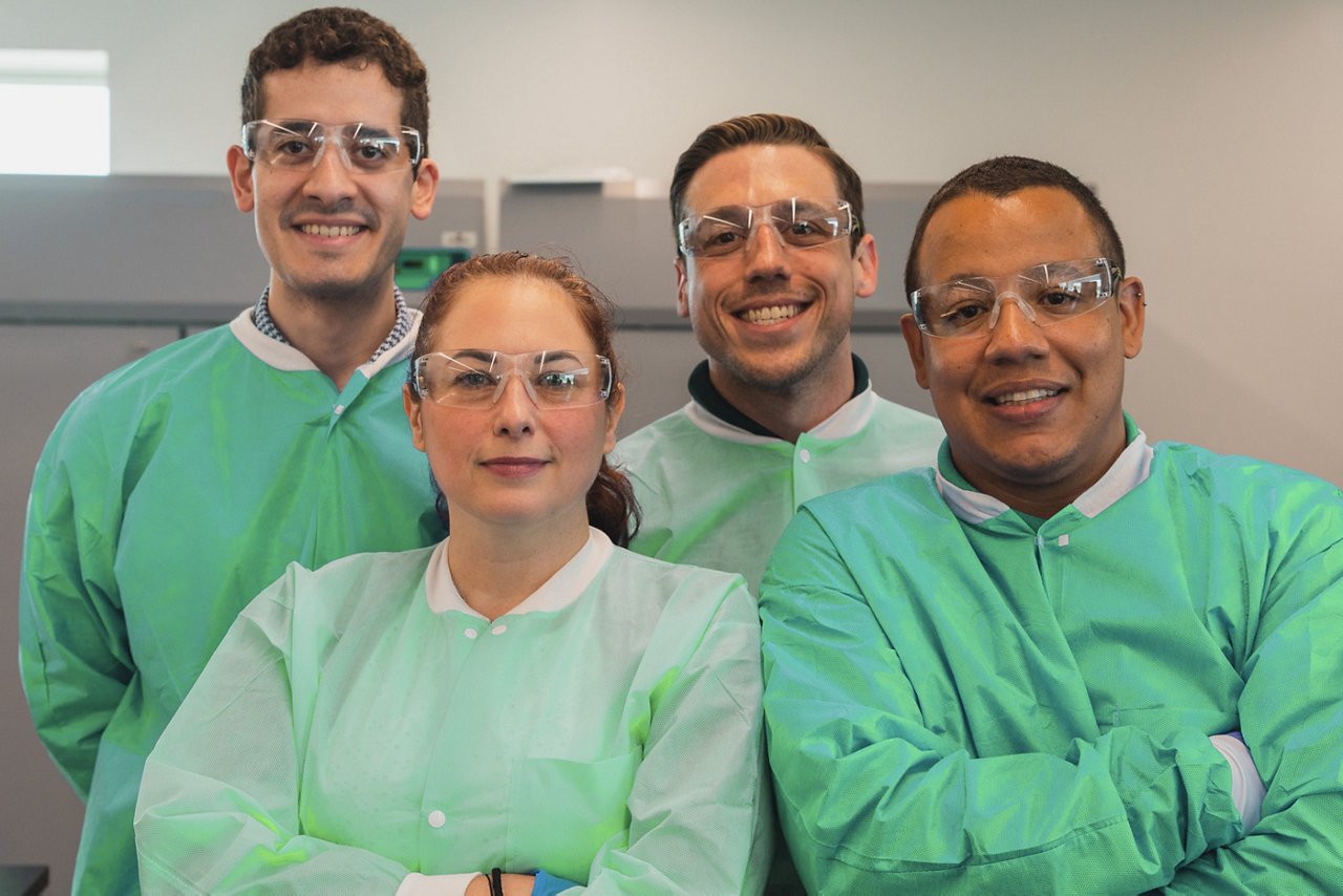 Four smiling scientists look directly into the camera, three male, one female