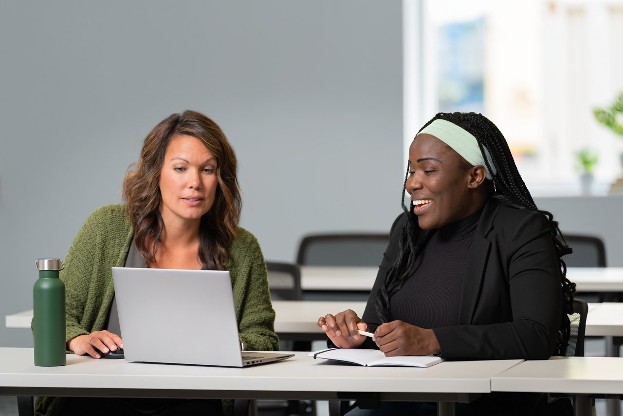 Two women employees meeting in a conference room while looking at a laptop computer.