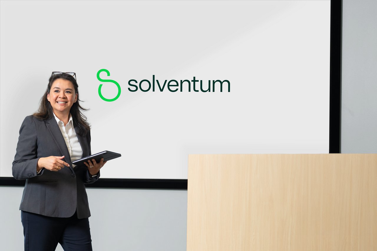 Mitarbeiterin bei einer Präsentation in einem Konferenzraum vor einem Podium und einem Bildschirm mit dem Solventum-Logo.