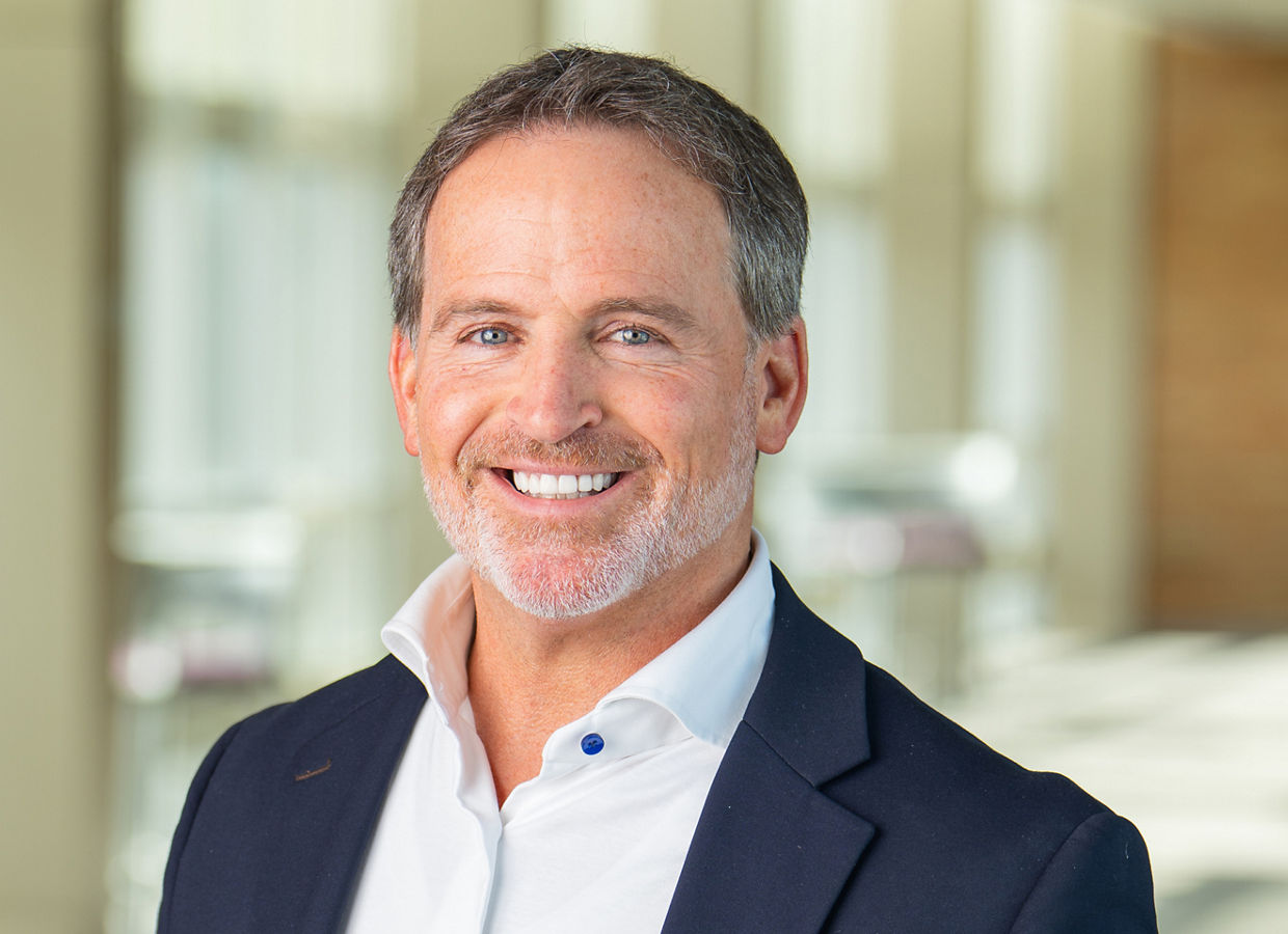 Chân dung của một người đàn ông, Bryan Hanson, Giám đốc điều hành của Solventum, đang mỉm cười và mặc một chiếc áo khoác Lam và áo sơ mi Màu trắng.