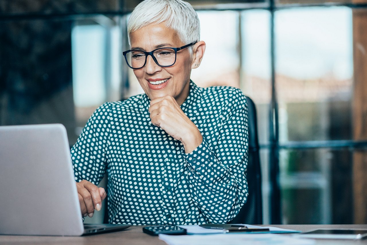 A businesswoman smiling whilst working on a laptop.