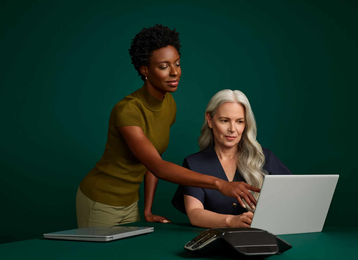 Portrait of a female coding director and hospital administrator reviewing an online document at a desk computer on a dark green background.