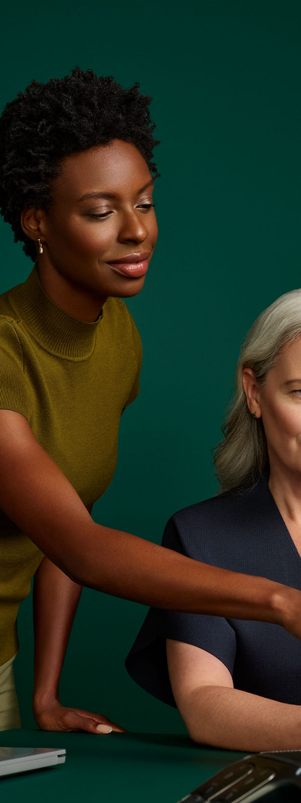 Portrait of a female coding director and hospital administrator reviewing an online document at a desk computer on a dark green background.